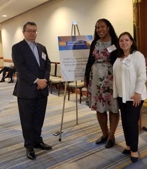Three professionals standing next to a tripod with a banner noting an event