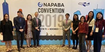 Nine professionals standing in front of a NAPABA Convention Banner